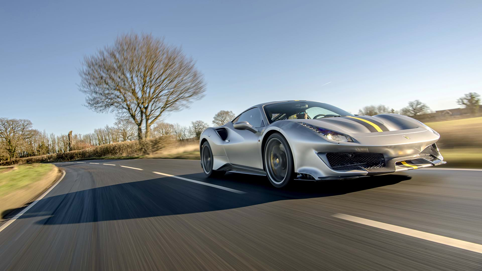 Gris élégant Ferrari 488 Pista avec une rayure de course audacieuse qui traverse un paysage champêtre pittoresque. 